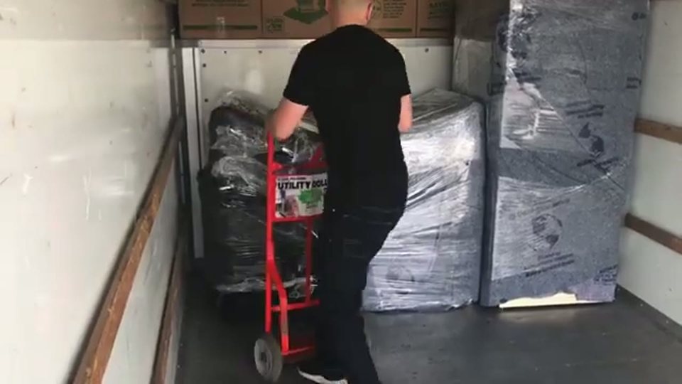 a mover loading shrink-wrapped mattresses into the truck with a hand truck