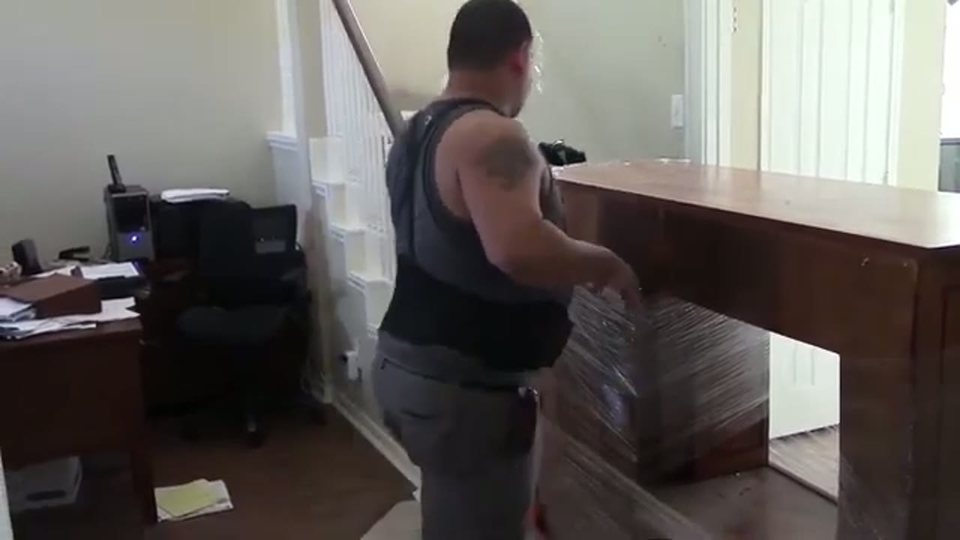 mover shrink-wrapping a large wood entertainment console beside a staircase