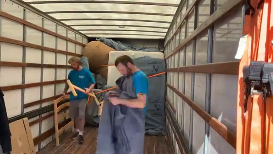 two movers arranging blanket-wrapped furniture inside the moving truck