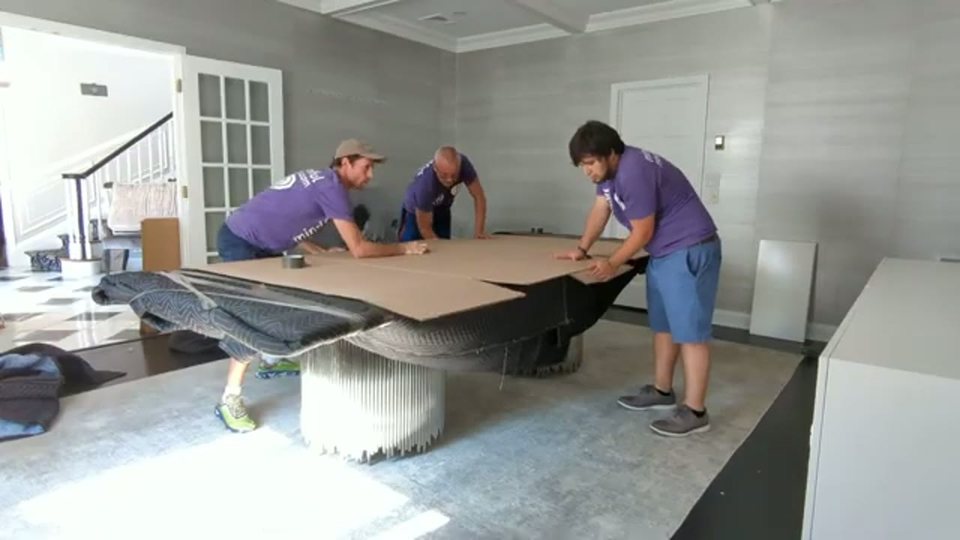 three movers sliding cardboard over a large glass dining table, face visible