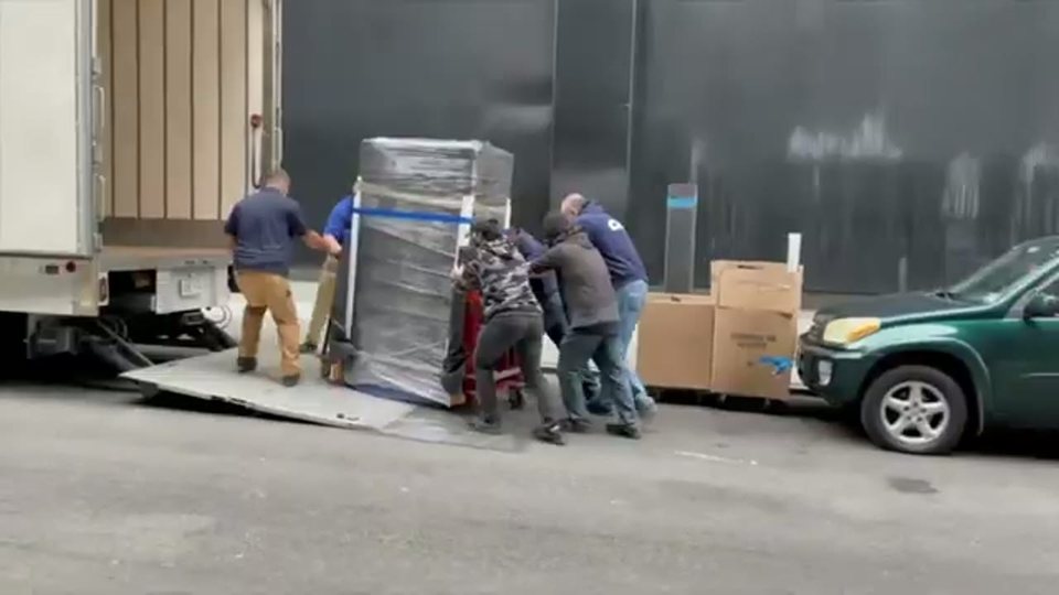 movers rolling a shrink-wrapped appliance up the ramp into the truck
