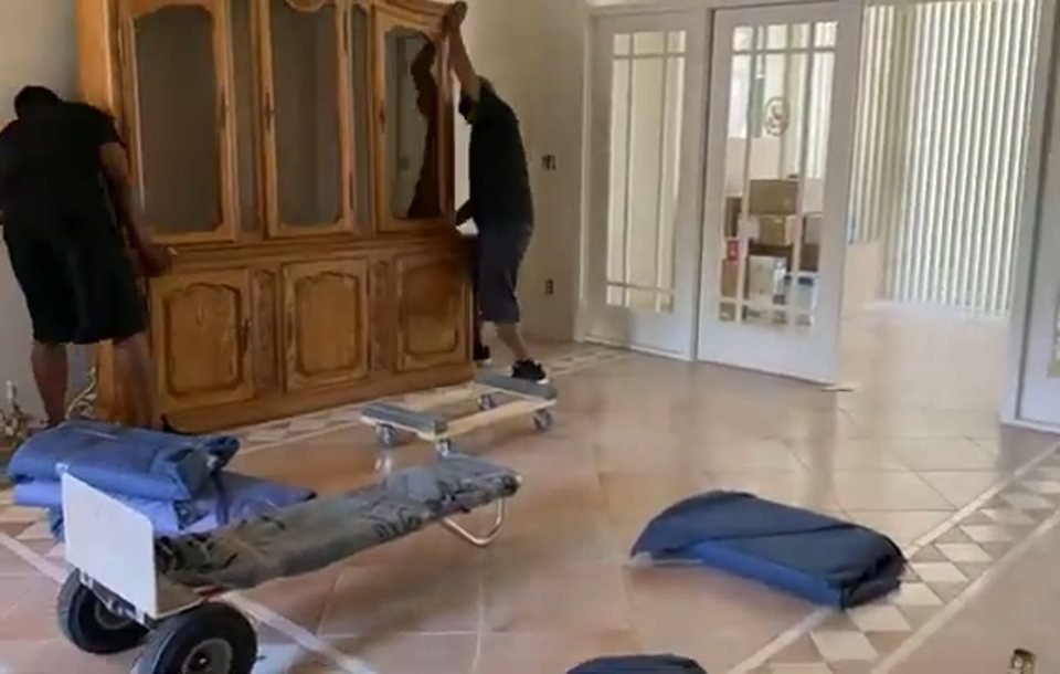 movers guiding a large china cabinet on a dolly across a living room