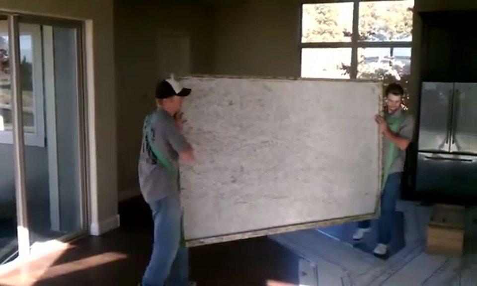 two movers carrying a large shrink-wrapped panel through a doorway