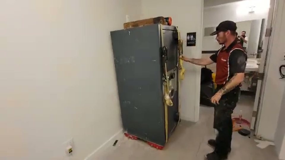 two movers relocating a tall wrapped appliance inside a home