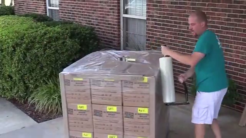 a mover shrink-wrapping a stacked pallet of moving boxes